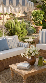 Outdoor seating area with wicker furniture, striped canopy, and a wooden table with flowers and books.