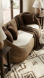 Wicker chair with brown cushions and a blanket on a patterned rug in a room.