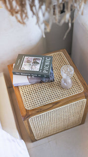 Wooden side table with wicker top featuring a book and glass.