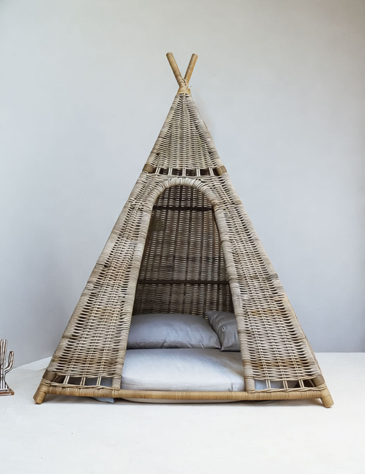 Wicker teepee with cushions on a white surface against a light gray wall