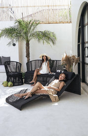 Two women relaxing on outdoor furniture with a palm tree and white wall in the background