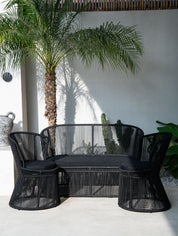 Black outdoor furniture set with a palm tree and white wall in the background