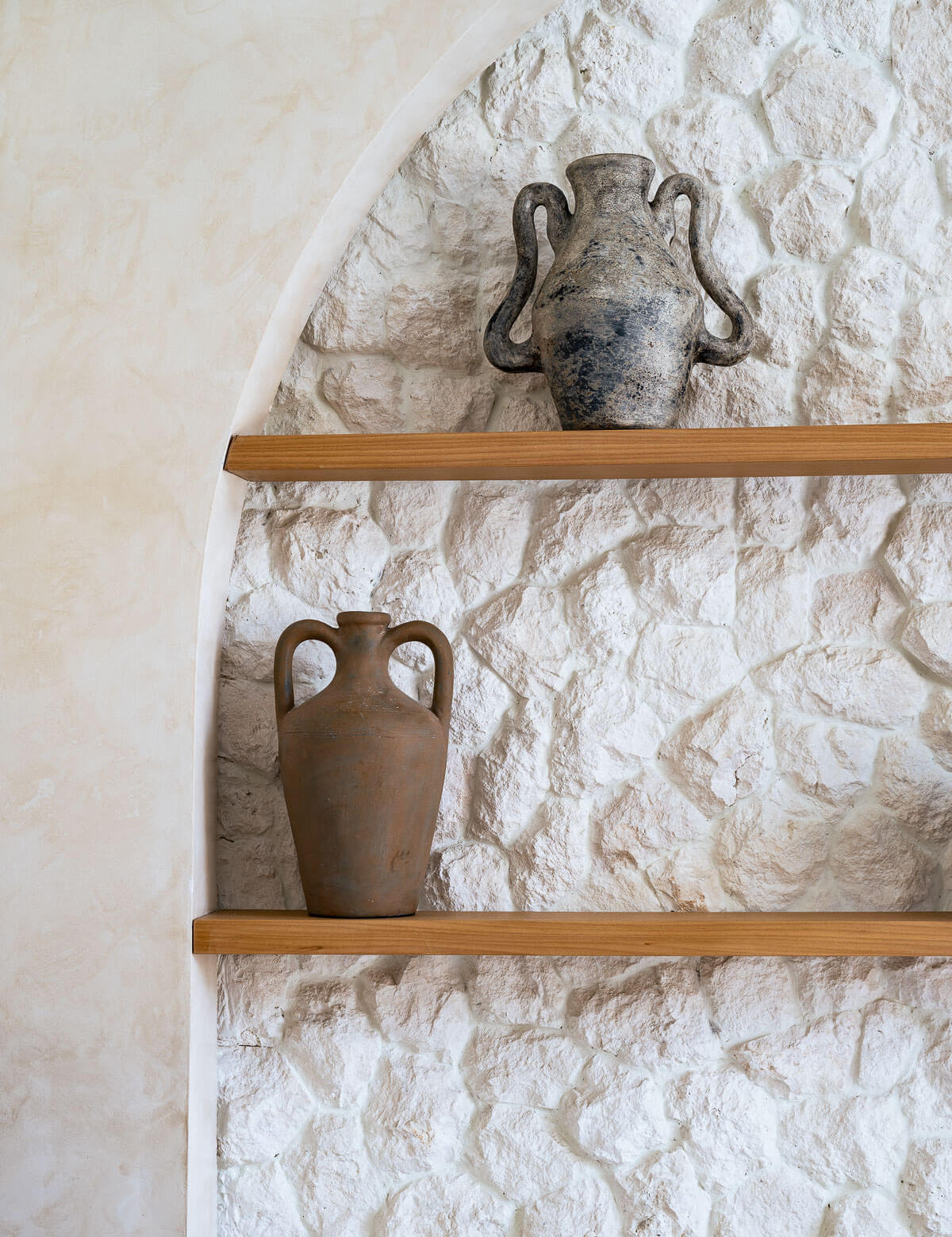 Two ceramic vases on wooden shelves against a textured stone wall.