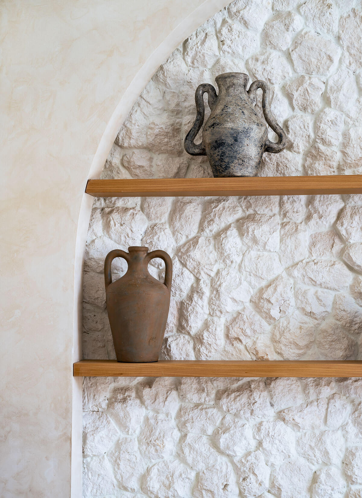 Two ceramic vases on wooden shelves against a textured stone wall.