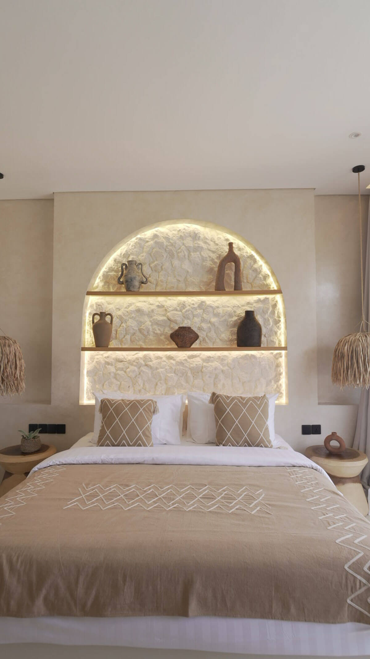 Neatly made bed with decorative pillows in a bedroom setting with wall-mounted shelves.