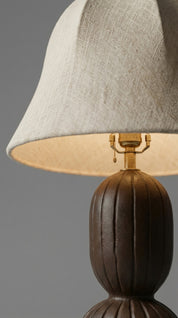 Close-up of a lamp with a textured brown base and gray lampshade on a gray background