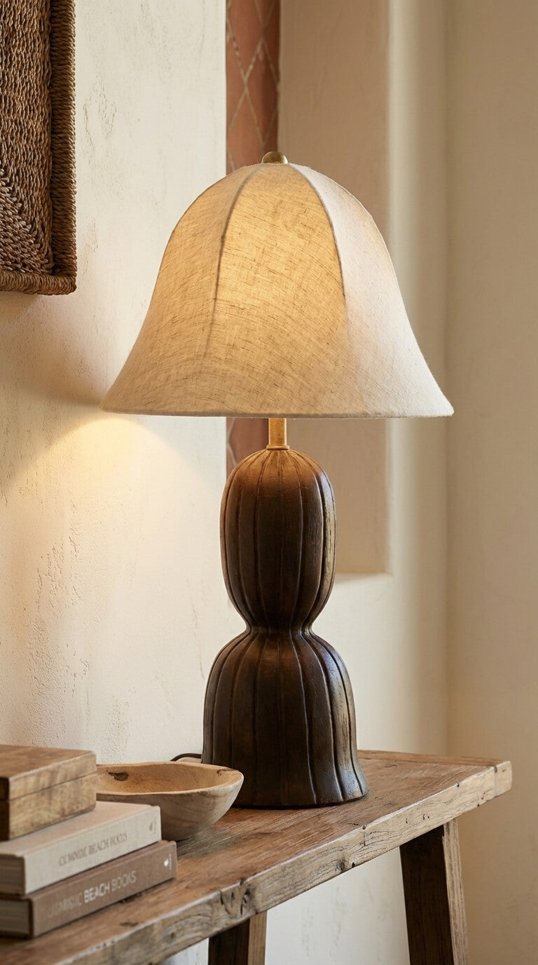 Table lamp with a beige shade on a wooden table against a neutral wall.