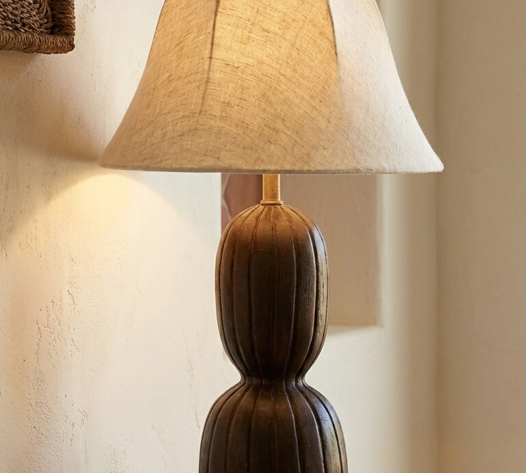 Table lamp with a beige shade on a wooden table against a neutral wall.