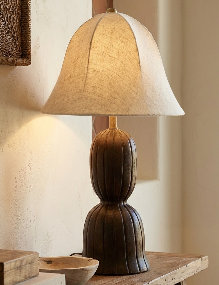 Table lamp with a beige shade on a wooden table against a neutral wall.