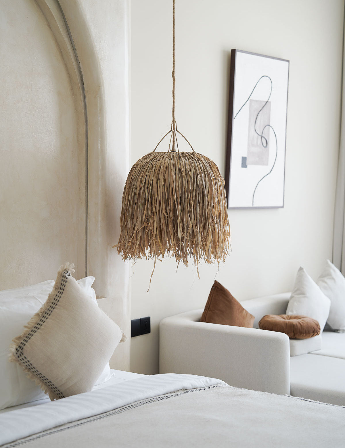 Woven pendant light hanging above a bed in a bedroom with neutral decor.