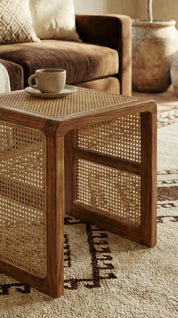 Wooden side table with wicker design next to a sofa with a cup on a saucer.