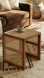 Wicker side table with a cup of coffee on a patterned rug in a living room.