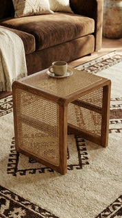 Wicker side table with a cup on a patterned rug in a living room.