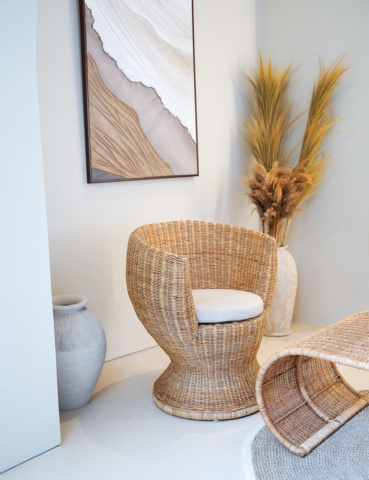 Wicker chair with a white cushion in a room with abstract art and decorative plants.