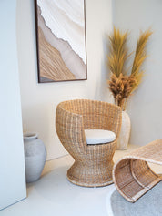 Wicker chair with a white cushion in a room with abstract art and decorative plants.