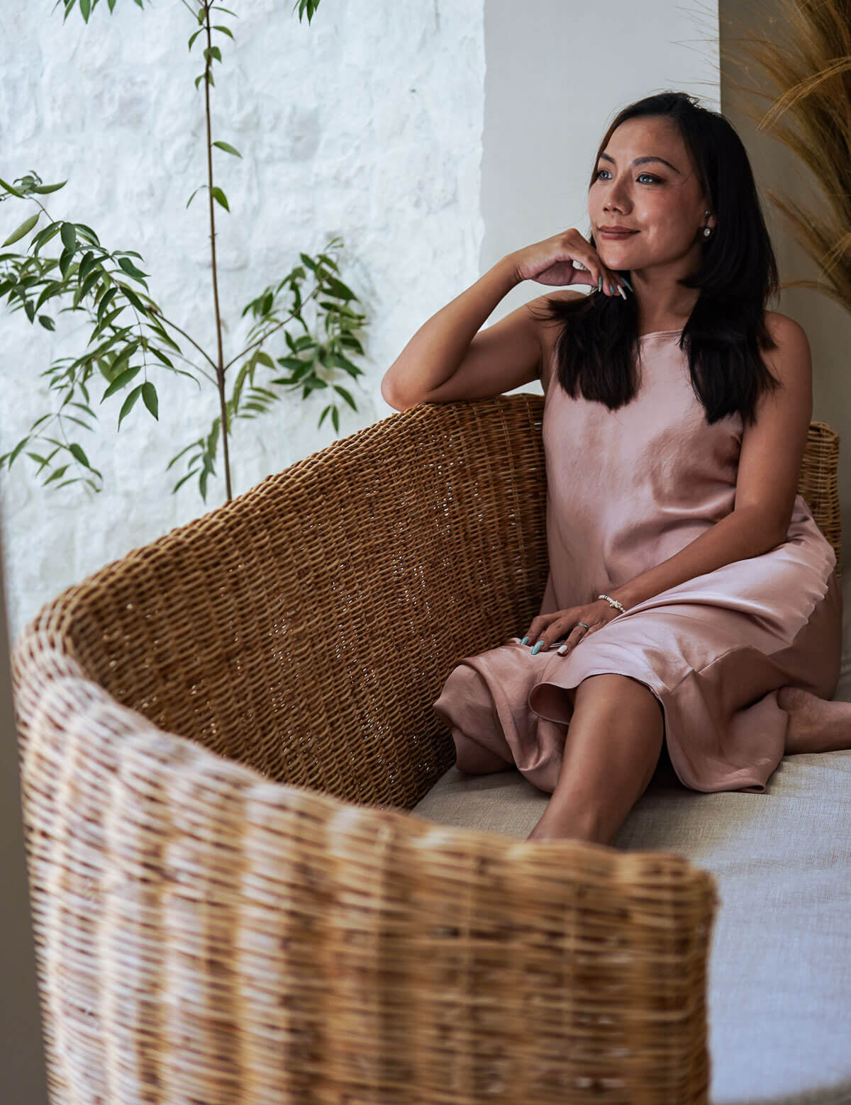Woman in a pink dress sitting on a wicker chair with plants in the background