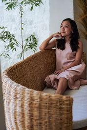 Woman in a pink dress sitting on a wicker chair with plants in the background