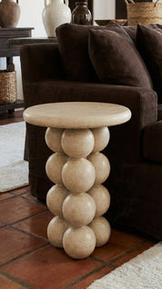 Round stone-styled side table in a living room setting with a brown sofa and decorative items.