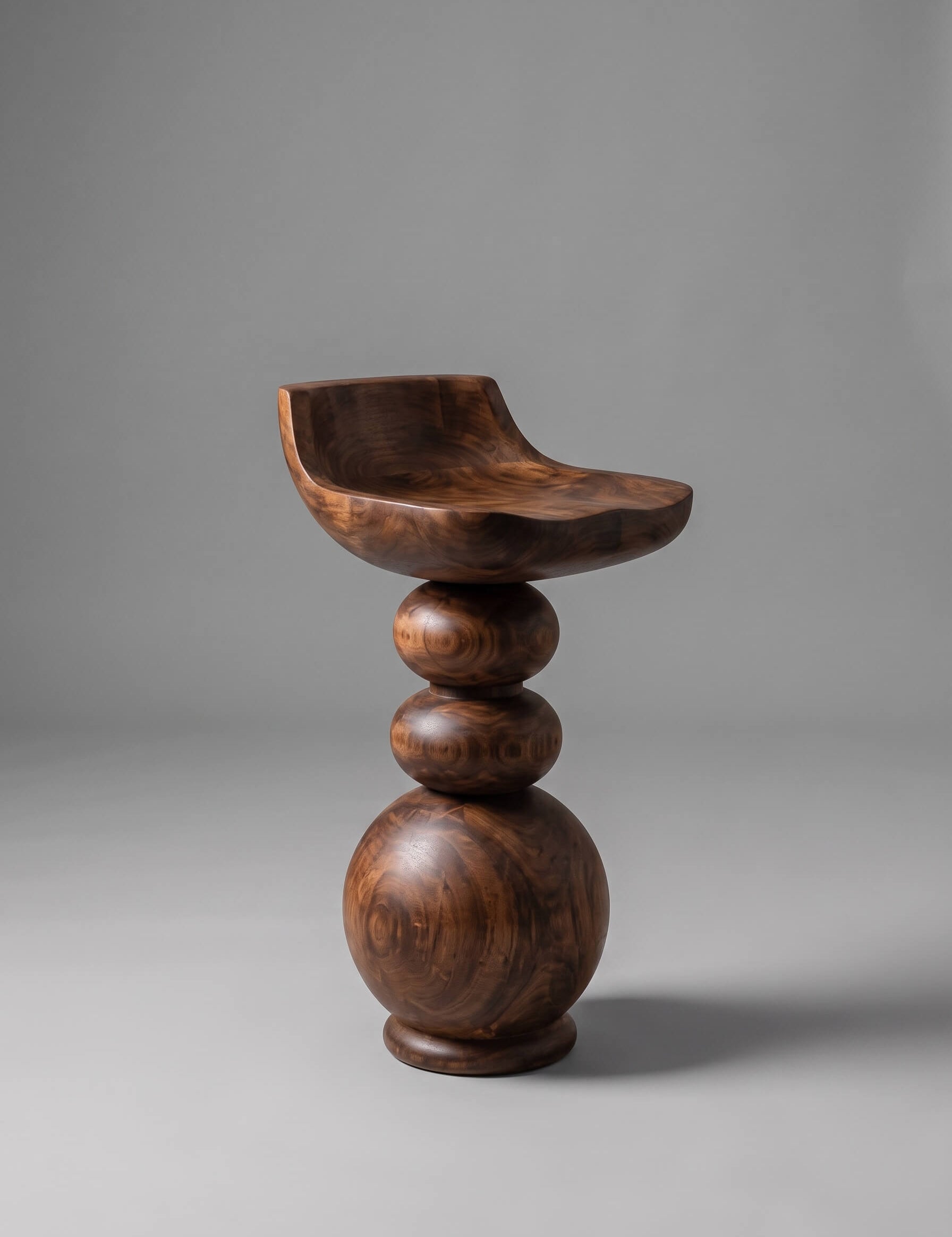 A sculptural wooden bar stool with a curved seat and stacked spherical legs, shown on a neutral gray studio background.