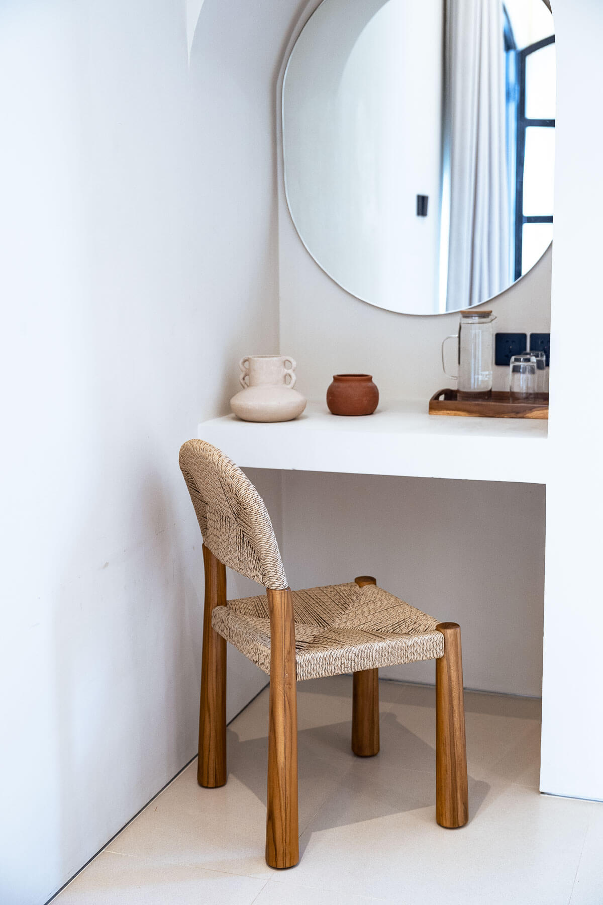 Wooden chair with woven seat and backrest in a room with a round mirror and decorative items on a desk.