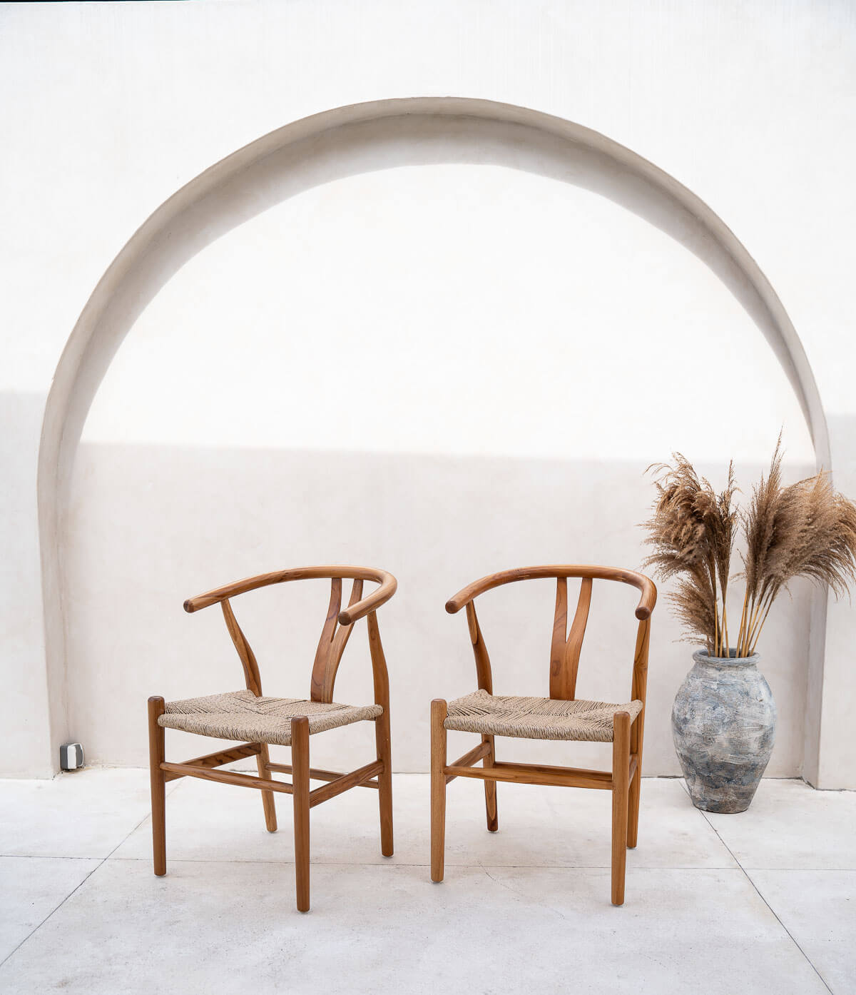 Two wooden chairs with woven seats under a concrete archway.