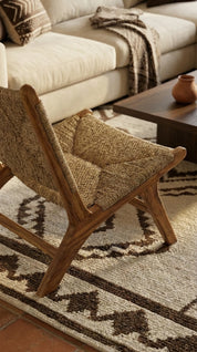Woven chair on a patterned rug with a couch and coffee table in the background