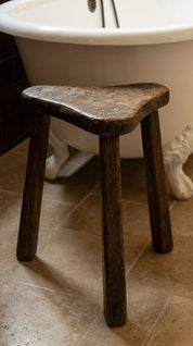 Wooden stool on a tiled bathroom floor with a bathtub in the background.