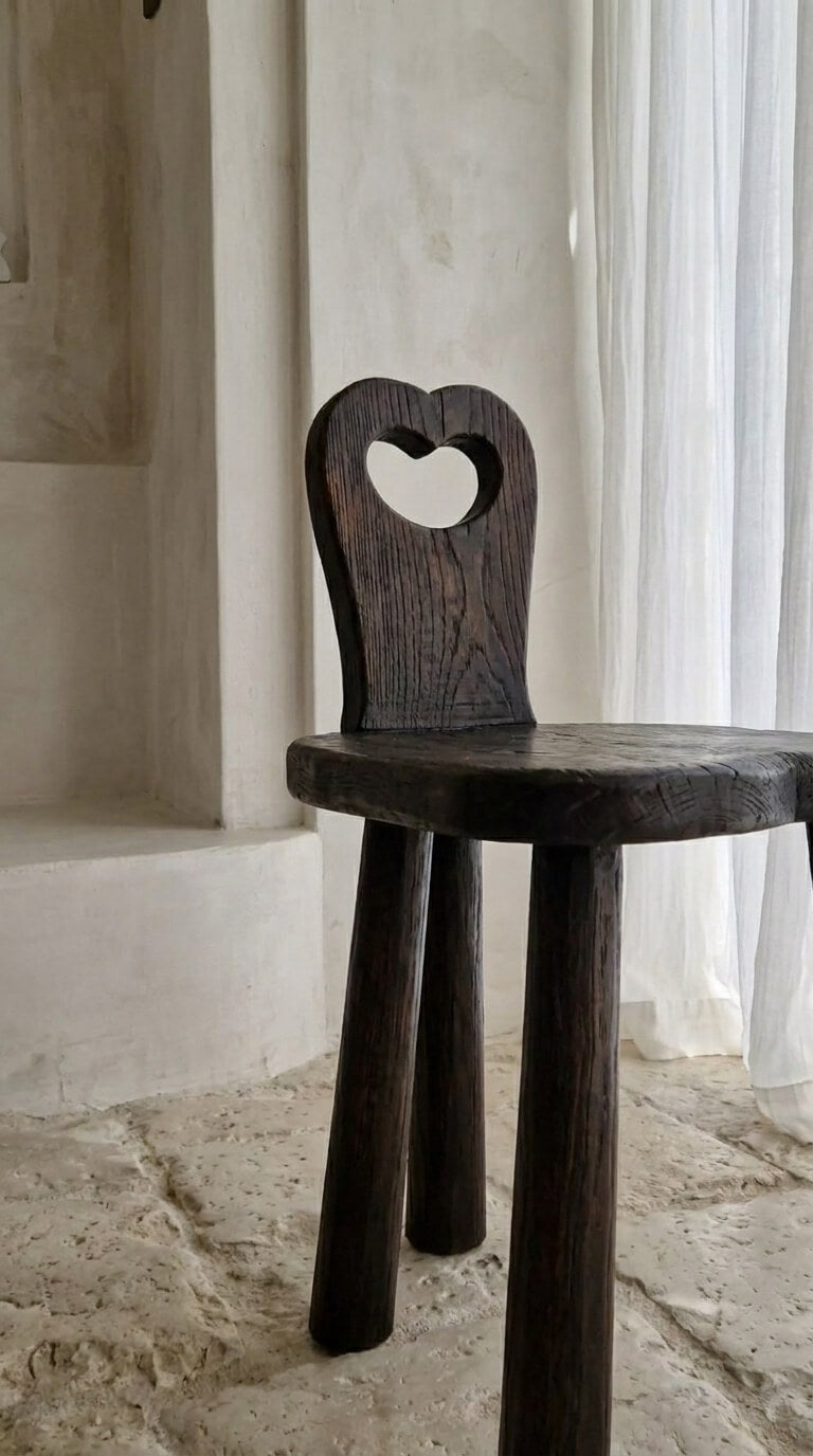 Dark wooden chair with heart-shaped backrest in a softly lit room.