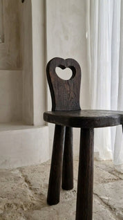 Dark wooden chair with heart-shaped backrest in a softly lit room.