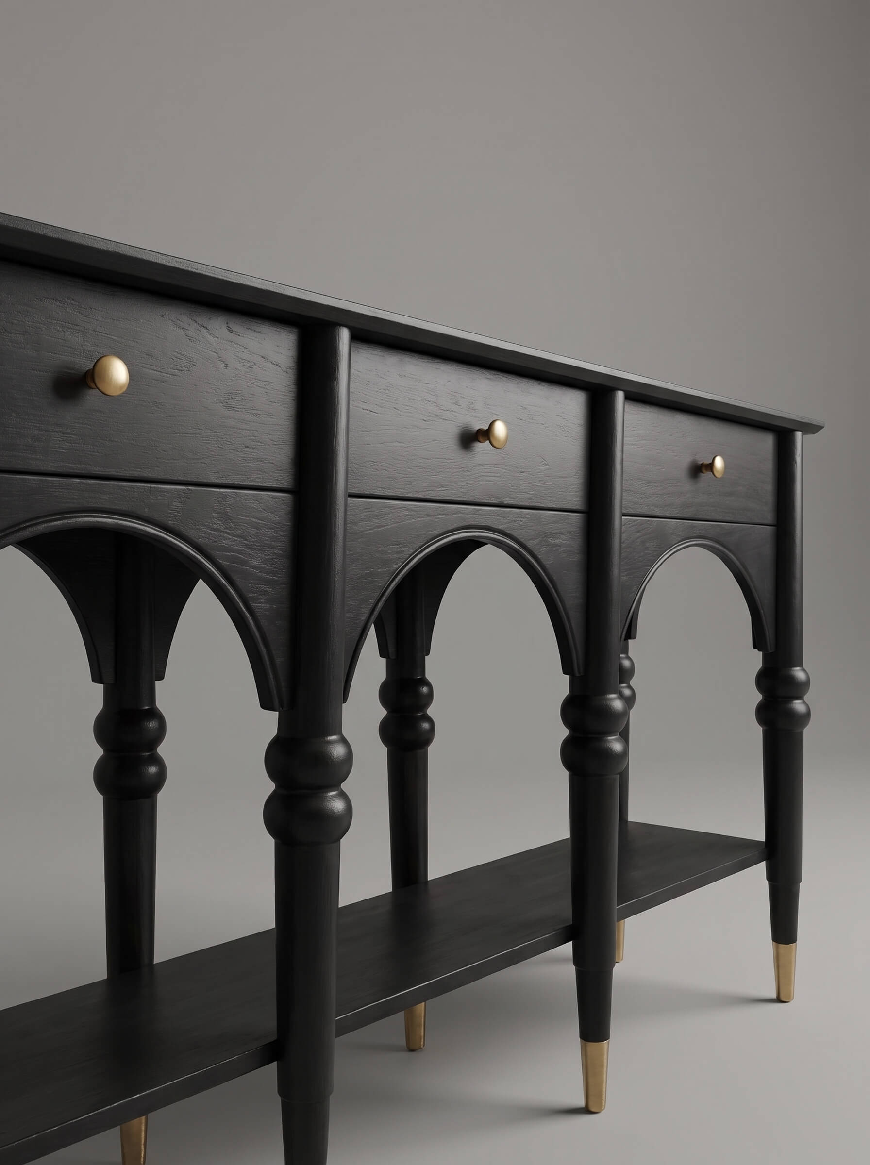 A black wooden console table with three drawers, arched legs, a lower shelf, and brass-finished drawer knobs and leg caps, photographed against a neutral gray studio background.