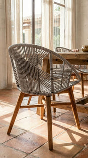 Wicker chair with wooden legs in a room with large windows and tiled floor.