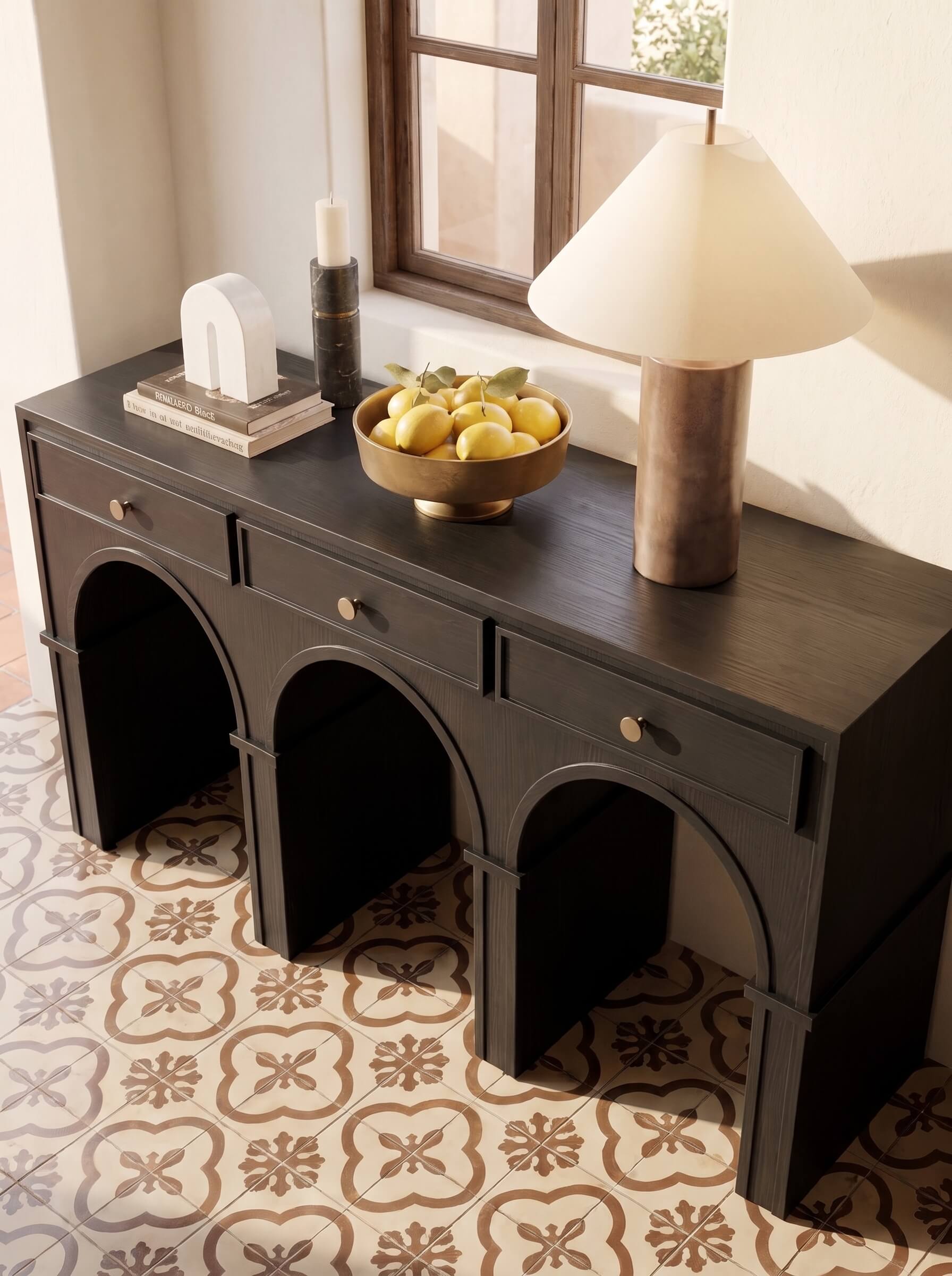A dark wood console table with three arched legs and small drawer pulls, styled in a room with patterned tile flooring, a window, a table lamp, and decorative objects on top.