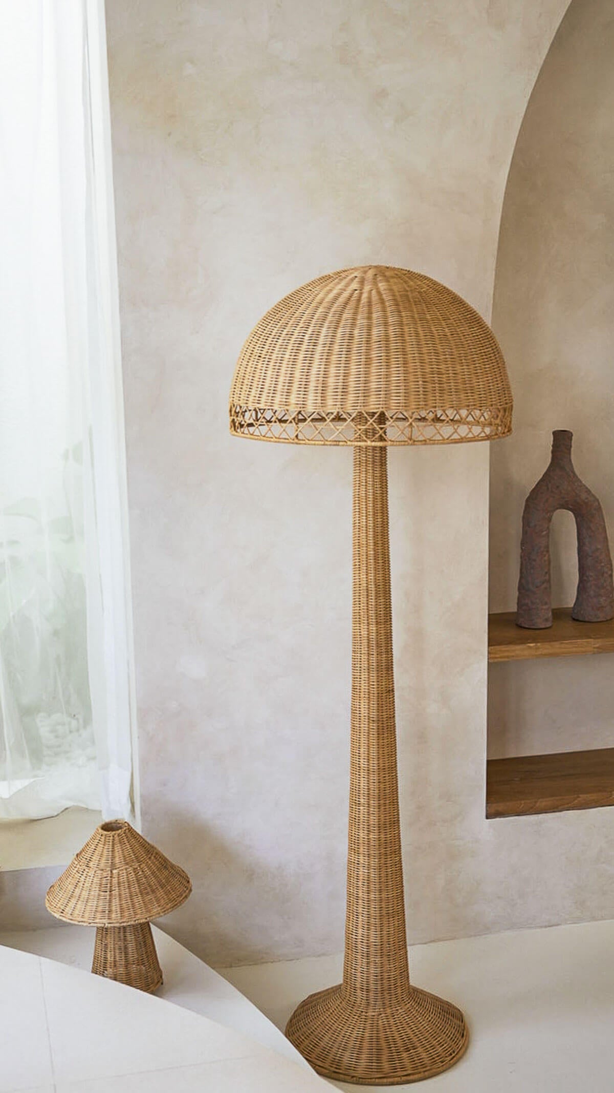 Wicker floor lamp in a room with neutral walls and a shelf.